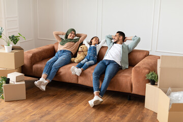 Family relaxing on couch in new home with cardboard boxes