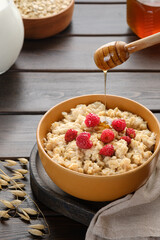 Healthy breakfast, homemade classic oatmeal porridge with raspberries, strawberries and honey next to ear of oats lying on the table. Vegan and vegetarian food.
