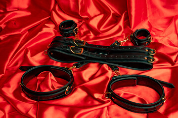Adult sex games. BDSM items. Leather straps handcuffs and gag ball on a red satin sheet.