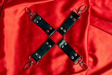 Adult sex games. BDSM items. Leather straps handcuffs on a red satin sheet.