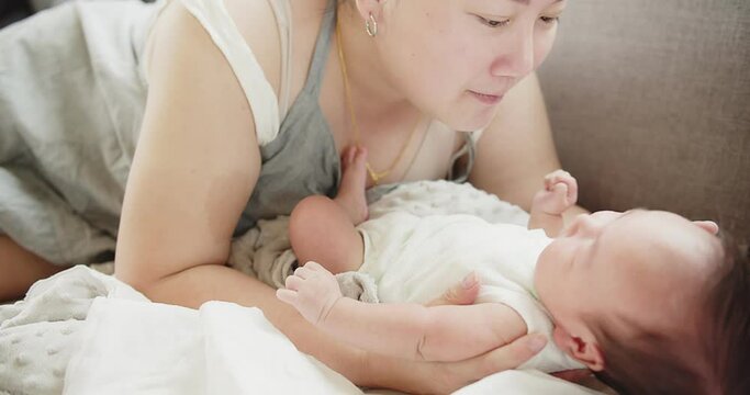 happiness family young Asian mother playing holding and kissing with her pretty newborn baby infant girl lying on bed at home, children, parenthood, childhood, life, maternity, motherhood love concept