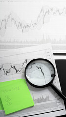 Financial instrument movement charts on white sheet of paper, magnifying glass on rebound chart,...