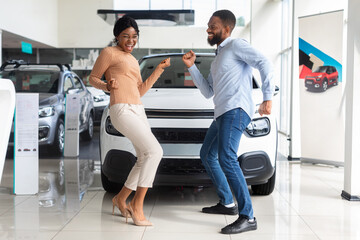 Fototapeta na wymiar Excited African American Spouses Dancing In Dealership Office After Buying New Car