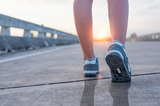 close-up photo of running shoes where the feet are on an empty road As the sun emphasizes the distance.