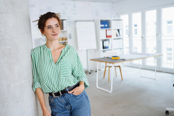 Cute young woman standing daydreaming in an office