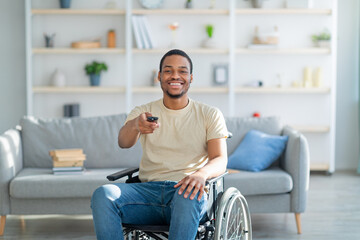 Home entertainments. Happy disabled African American guy with TV controller enjoying movie indoors