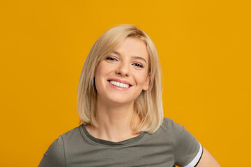 Female portrait. Happy young woman with blonde hair looking at camera and smiling, posing in studio, yellow background