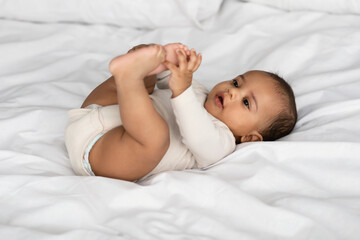 Cute little African American infant lying in bed and playing