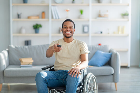 Home entertainments. Happy disabled African American guy with TV controller enjoying movie indoors