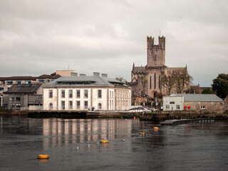 Naklejka premium Limerick City District Court building and St Mary's Cathedral. Ireland. Reflection in river Shannon. Popular town landmark and tourist spot. Cloudy sky.