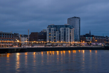 Fototapeta premium Riverside area at night. Shannon river, Limerick city, Ireland. Blue and orange colors. Dusk scene. Cloudy sky. Christmas and New Year illumination.
