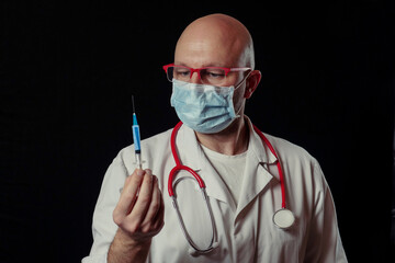 Portrait of a bald doctor with syringe full with blue color vaccine. Dark background. Selective...