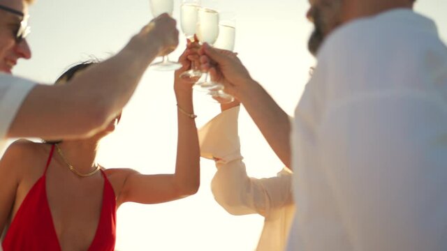Group of man and woman friends enjoy party drinking champagne with talking together while catamaran boat sailing at summer sunset. Male and female relax outdoor lifestyle on tropical travel vacation