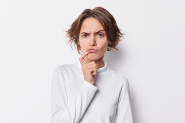 Beautiful serious young woman looks with serious suspicious expression raises eyebrows keeps finger...