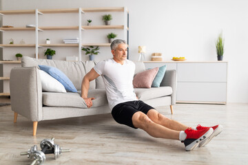 Fototapeta na wymiar At home workout routine. Sporty mature man leaning on sofa and doing push-up exercises, working out in living room