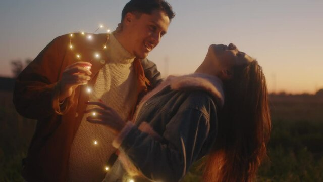 Giovane coppia di ragazzo e ragazza si bacia con striscia di luci led al tramonto