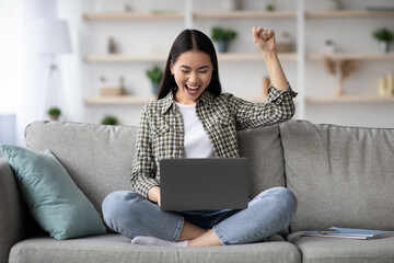 Naklejka premium Emotional asian woman with laptop celebrating success