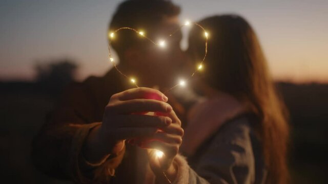 Giovane coppia di ragazzo e ragazza si bacia con striscia di luci led al tramonto