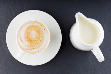 Cup of coffee on a dark background. Coffee on a slate board. Cup of morning coffee on a white saucer. Top view. Copy space
