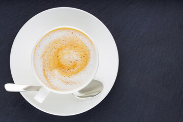 Cup of coffee on a dark background. Coffee on a slate board. Cup of morning coffee on a white saucer. Top view. Copy space