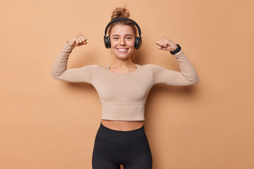 Horizontal shot of active slim young woman raises arms shows biceps after workout dressed in...