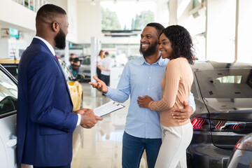 Fototapeta premium Family Buying Car. African American Spouses Purchasing New Vehicle In Dealership Center