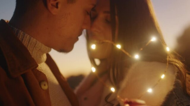 Giovane coppia di ragazzo e ragazza si bacia con striscia di luci led al tramonto
