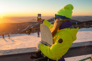 girl photographing the sunset on a mobile phone at the top of a mountain ski resort
