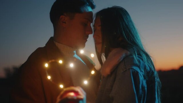 Giovane coppia di ragazzo e ragazza si bacia con striscia di luci led al tramonto