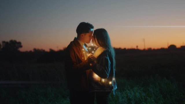 Giovane coppia di ragazzo e ragazza si bacia con striscia di luci led al tramonto