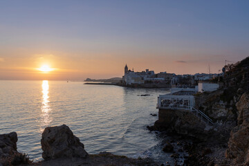Naklejka premium A scenic sunset is reflected in the Mediterranean Sea, with the city of Sitges in the background.
