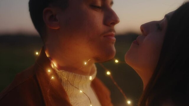 Giovane coppia di ragazzo e ragazza si bacia con striscia di luci led al tramonto