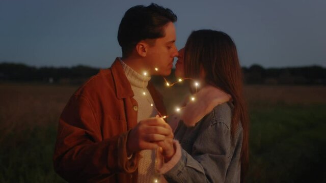 Giovane coppia di ragazzo e ragazza si bacia con striscia di luci led al tramonto
