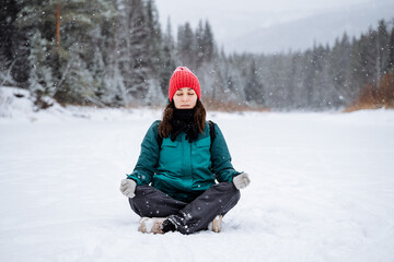 Fototapeta na wymiar A young girl meditates in a snowy valley. A woman sits in a pose and catches Zen. A walk in the forest in winter, filled with peace, tranquility and joy