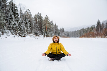 Fototapeta na wymiar Curly man meditates in a snowy valley. Cheerful man sits in a pose and catches Zen. A walk in the forest in winter, filled with peace, tranquility and joy