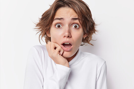 Headshot of frightened impressed woman with dark short hair holds breath from amazement keeps jaw dropped hears something shocking dressed casually isolated over white background. Omg concept
