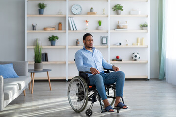 Fototapeta na wymiar Full length of impaired African American guy suffering from disability depression, sitting in wheelchair at home