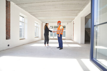 Woman construction engineer shaking hands with worker in room