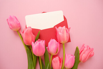 Pink tulip flowers composition with blank greeting card on pink background. Valentine's day, Mother's day, Women's day and spring greeting concept floral layout.