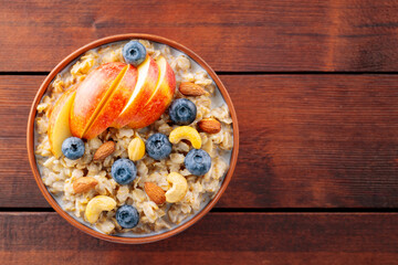 Oatmeal with blueberries, apple and nuts. Bowl of oatmeal porridge on wooden boards. Healthy breakfast concept. Top view. Copy space