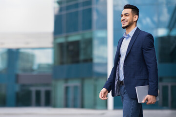 Happy young arab businessman walking from office, holding notepad
