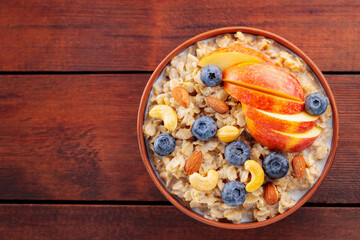 Oatmeal with blueberries, apple and nuts. Bowl of oatmeal porridge on wooden boards. Healthy breakfast concept. Top view. Copy space
