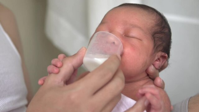 Father feeding milk with cup to him son baby. Asian man feeding milk kid infant. Relationship love family concept. 