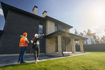 Woman pointing at upper floor of house to worker