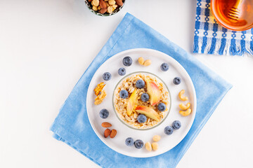 Oatmeal porridge with blueberries and sliced apple in bowl. Oatmeal with berries, nuts and honey on a white background. Healthy breakfast. Top view