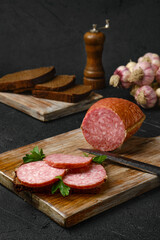 Smoked salami and sandwich on cutting board over black background