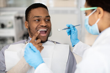 Black Male Patient Showing Aching Tooth During Check Up With Female Dentist