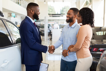 Sales Manager Helping Black Couple Choose New Car In Modern Dealership Center