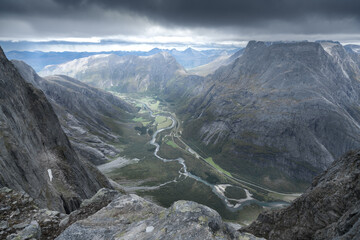 View from the top of Trollveggen, or Troll Wall, in Norway. Famous viewpoint in Norwegian mountains. Dramatic mountain range on a cold and cloudy day of autumn. Winding river in the valley below.