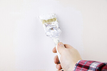 The builder paints the wall with white paint. The painter holds a brush for painting the walls